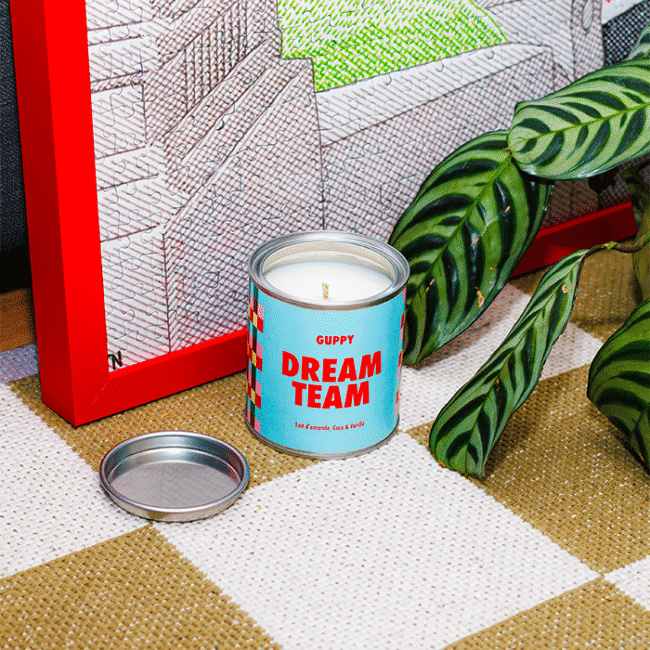 Bougie parfumée Dream Team en vue plongée sur un tapis, avec une plante et un puzzle en fond
